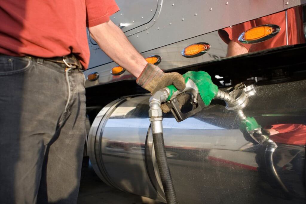 Commercial truck driver fueling semi truck at fuel station for IFTA reporting and fleet vehicle data tracking
